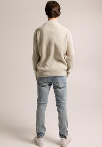 Beige ribbed sweater with a crew neck and long sleeves, paired with light blue slim-fit jeans and white sneakers. View from the back.