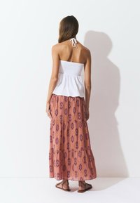 Top halter blanco con fruncidos, combinado con una falda larga y fluida de color rosa con un patrón de acentos morados. Se lleva con sandalias marrones.