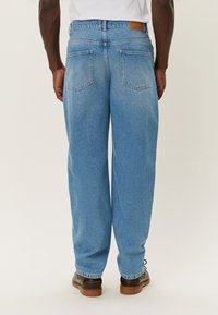 Light blue denim jeans with a relaxed fit, featuring two back pockets and a brown leather patch at the waist. Smooth texture and classic design.