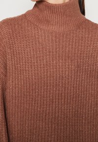 Maglione a collo alto color ruggine con texture a coste, caratterizzato da un colletto alto e una vestibilità ampia. Tessuto lavorato a maglia morbido. Senza chiusure visibili.