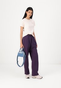Ljusrosa t-shirt med liten grafik, löst sittande lila sweatpants och en liten blå handväska med axelrem. Avslappnade skor ingår.