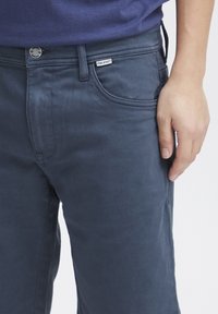 Temno modri hlače slim fit, z sprednjim žepom, z gumbom za zapiranje in označenim pasom. Gladka tekstura tkanine.