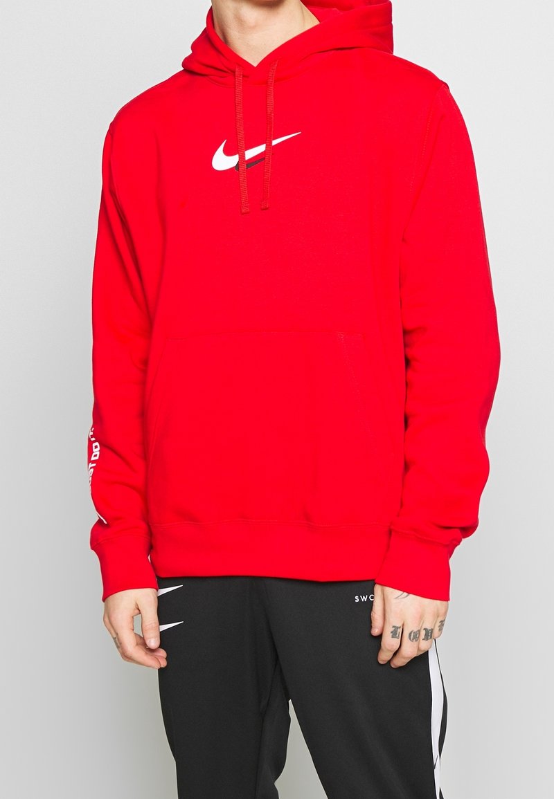 Röd Nike-hoodie med en framficka, dragsko i huvan och en vit swoosh-logga på bröstet. Långa ärmar med tryckta detaljer.