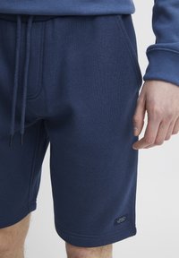 Námornícke modré bavlnené šortky s elastickým pásom, detaily so šnúrkou, bočnými vreckami a malou dekoračnou nášivkou pri leme.