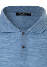 Světle modrá polo košile s texturovanou tkaninou, dvěma tmavými knoflíky a měkkým límcem. Označení zní "MAERZ Muenchen."