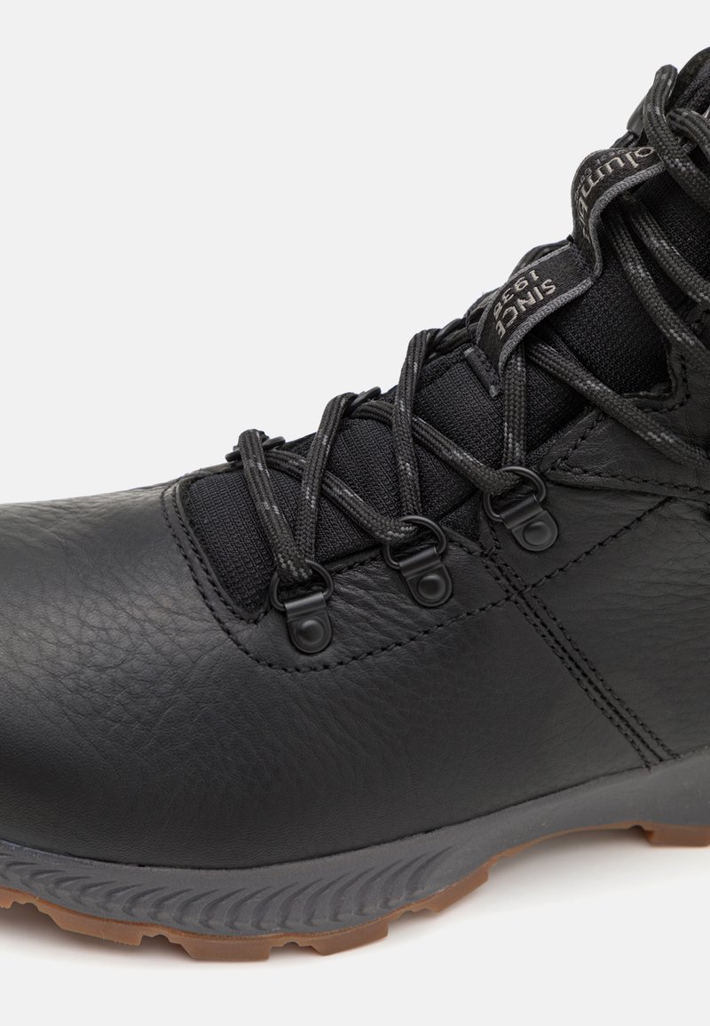 Bota de senderismo negra de cuero con una superficie texturizada, que presenta un sistema de cordones de tela negra, suela de goma y acentos grises en la suela.
