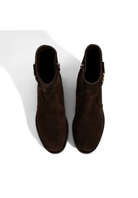 Braune Wildleder-Stiefeletten mit runder Spitze, flacher Sohle und Knöchelhöhe. Mit einem seitlichen Reißverschluss und goldfarbenen Hardware-Details.