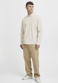 Lyse beige stribet langærmet skjorte med krave og knapper, parret med tanfarvede bukser og hvide sneakers. Glat stof, almindelig pasform.