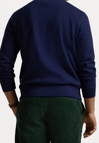 Mörkblå sweatshirt med ribbade muddar och fåll, kombinerad med mörkgröna kordbyxor med en subtil struktur. Inga anmärkningsvärda mönster eller grafik.