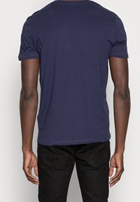 Camiseta de algodón azul marino con mangas cortas, cuello redondo y textura suave. La vista trasera muestra un diseño simple sin patrones ni adornos.