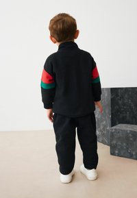 Black sweatshirt with red and green striped accents on sleeves, paired with matching black sweatpants and white sneakers. Soft fabric, relaxed fit.