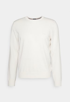 Ljus krämfärgad rundhalsad tröja i mjukt tyg, med långa ärmar, ribbade muddar och en diskret logotyp på bröstet.