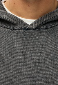 Gros plan sur une personne portant un hoodie en tricot gris sur une chemise blanche, montrant le décolleté et la partie supérieure de la poitrine.