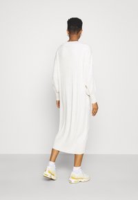 Abito bianco a coste con maniche lunghe e vestibilità rilassata, che arriva a metà polpaccio, abbinato a sneaker beige e calzini bianchi a collo.