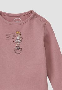 Rosa Baumwollhemd mit langen Ärmeln, das eine Kindergrafik eines Mädchens auf einem Einrad zeigt, mit dem Text "ICH KANN ALLES MACHEN" und kleinen Herzen.