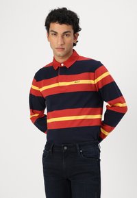 Langærmet polo-shirt i navy med røde og gule vandrette striber, med krave, knaplukning og lille brandlogo.