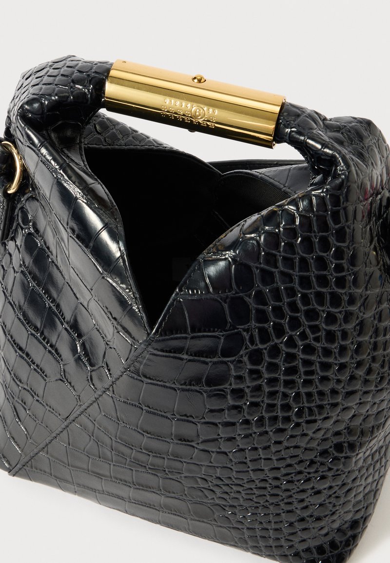 Sac en cuir noir embossé crocodile avec une poignée en métal doré. L'ouverture supérieure révèle un intérieur lisse. Présente un design structuré et angulaire.