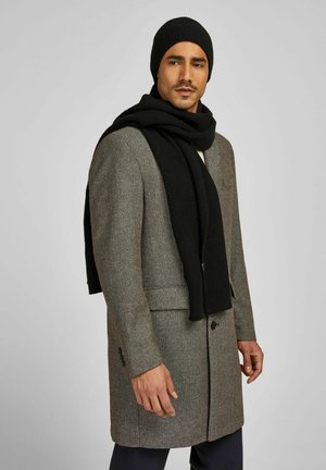 Grauer Wollmischmantel mit Reverskragen, zwei Fronttaschen, kombiniert mit einer schwarzen, gerippten Strickmütze und einem Schal. Glatte Textur, maßgeschneiderte Passform.