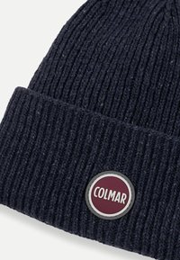 Căciulă din tricot ribat albastru închis, cu tiv pliat și patch rotund albastru burgund și alb al brandului Colmar cusut în față.