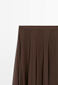 Bruine geplooide rok met een aansluitende tailleband, vloeiende stof en verticale paneeldetails tegen een effen witte achtergrond.