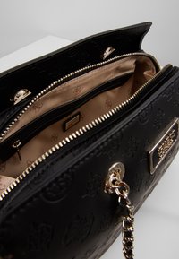 Sac à main en simili cuir noir avec un design embossé, quincaillerie dorée, compartiments zippés doubles et doublure en tissu beige avec un motif de logo.