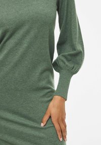 Grünes Strickkleid mit lässiger Passform, gerippten Bündchen und weicher Textur. Seitentaschen und sanfte Puffärmel sind bemerkenswerte Merkmale.
