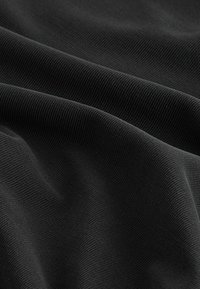 Schwarz gerippter Stoff mit einer sanften Textur, der ausgeprägte parallele Linien und eine leichte Dehnbarkeit aufweist, wodurch ein wellenartiges Aussehen entsteht.