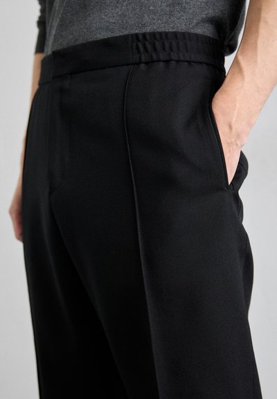 Pantalones negros con una textura suave, que cuentan con una cintura elástica, bolsillos laterales y líneas limpias para un ajuste entallado.