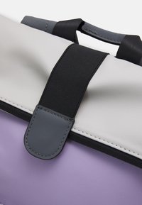 Sac rembourré gris et lavande avec une bandoulière en tissu noir et une fermeture à clip grise. Présente une texture lisse et des coutures contrastantes.