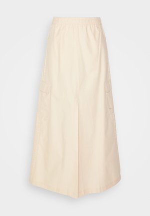 Fustă cargo bej cu talie elastică, buzunare laterale și o croială lejeră. Țesătura pare netedă, cu un ușor luciu.