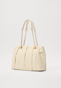 Πληθωρική τσάντα χρώματος κρέμα με διπλές αλυσίδες και δερμάτινους ιμάντες, που διαθέτει χρυσές λεπτομέρειες και μαλακή, υφασμάτινη υφή.