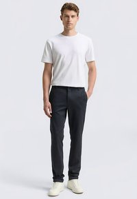 Biała koszulka z krótkim rękawem w połączeniu z ciemnoszarymi spodniami o prostym kroju i gładkiej fakturze, uzupełniona białymi trampkami.