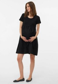 Abito da maternità nero con maniche corte, scollatura rotonda e vita arricciata per un maggiore comfort. Abbinato a scarpe basse nere.