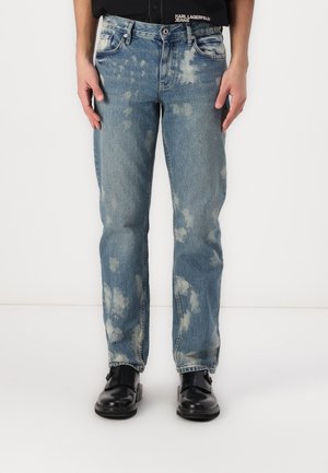 Straight-leg falmede blå jeans båret med sorte lædersko og en sort skjorte med synligt Karl Lagerfeld Jeans-mærke.