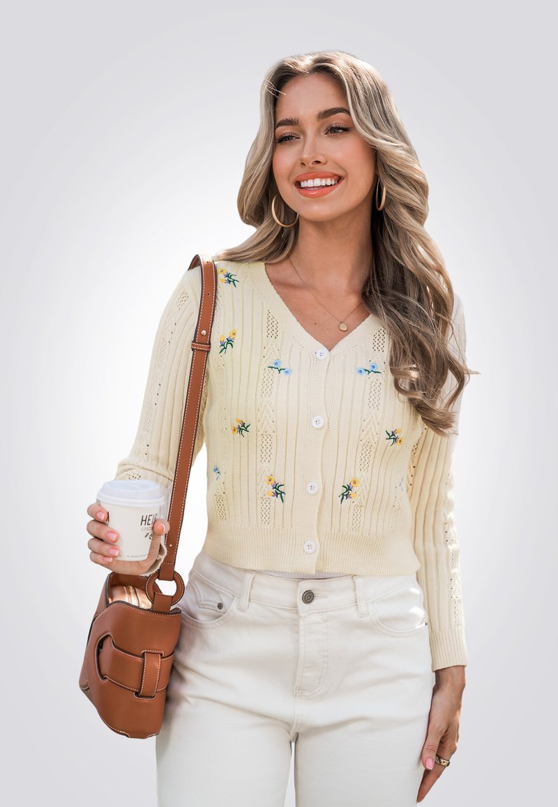 Crème gebreide cardigan met V-hals, bloemenborduurwerk en knoopsluiting. Gecombineerd met crème hoge taille jeans en een bruine schoudertas.