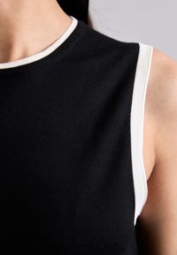 Top negro sin mangas con cuello redondo y ribete blanco, fabricado en un suave tejido texturizado. Diseño limpio, ajuste ceñido.