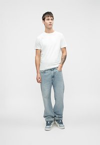 Λευκό βαμβακερό T-shirt, ανοιχτό μπλε φαρδιά τζιν και γκρίζα αθλητικά παπούτσια με μπλε λεπτομέρειες. Απλός σχεδιασμός με χαλαρή εφαρμογή και ελάχιστες λεπτομέρειες.