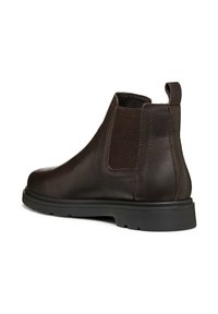 Bota de cuero marrón de tobillo con paneles laterales elásticos, puntera redondeada, tirador y acentos texturizados, reposando sobre una suela de goma negra.