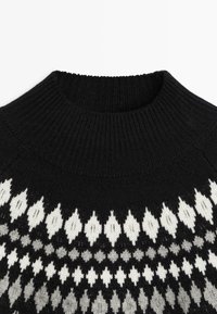 Zwarte gebreide trui met een geribde hoge hals en een geometrisch wit-grijs patroon aan de onderkant. Zachte textuur.