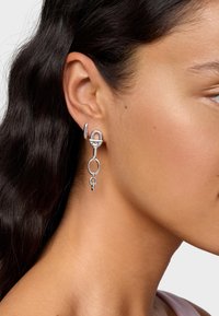 Silberne Ohrringe mit runden und ovalen Gliedern, glatter Oberfläche und elegantem Design, die an einer Steckerbefestigung nahe dem Ohr hängen.