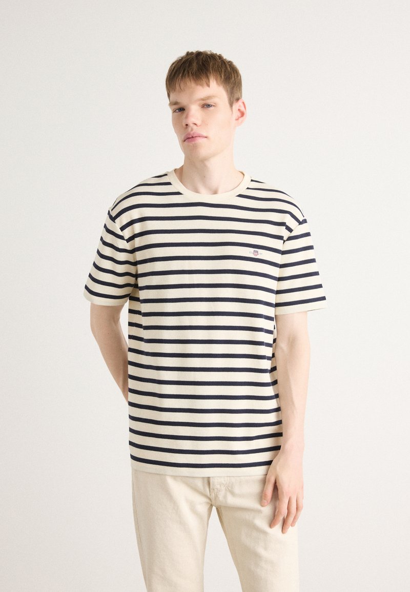 Striped t-shirt in cream and navy, featuring short sleeves and a crew neckline. Has embroidered logo detail on the chest.