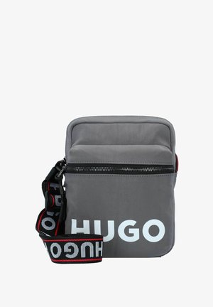 Bolso bandolera de nailon gris con cierre de cremallera, que presenta un destacado logo en blanco "HUGO" y una correa ajustable con un patrón negro y rojo.
