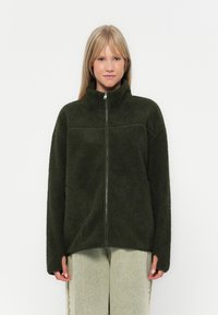 Giacca in fleece verde scuro con colletto alto e zip completa, caratterizzata da una superficie tessurizzata e una vestibilità comoda.