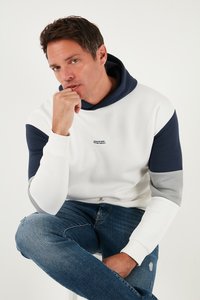 Hvid og marinefarvet farveblokket hoodie med grå accenter, der har en hætte med snoretræk og tekstdetalje på brystet. Kombineret med slidte blå jeans.