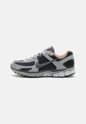 Szaro-czarny but biegowy Nike z białymi sznurówkami, amortyzowaną podeszwą, cholewką z siateczki oraz beżową, wyściełaną wyściółką wewnętrzną.