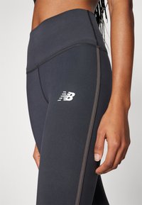 Čierne legíny s vysokým pásom, so bielym logom New Balance, kontrastným šedým prešívaním a priliehavým strihom.