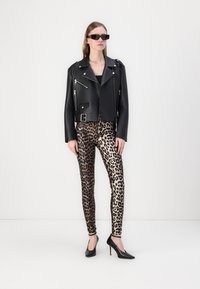 Crna kožna moto jakna sa srebrnim patentnim zatvaračima, uparena s tajicama leopard printa i crnim štiklama, prikazana na svijetloj pozadini.