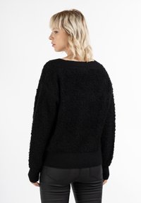 Sort, struktureret sweater med løs pasform og ribbede manchetter. Har en bred halsudskæring og et blødt, fluffy materiale til varme.