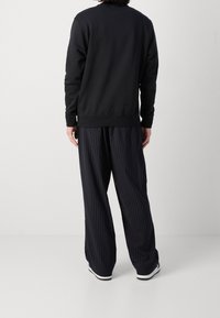 Sudadera negra con cuello redondo, combinada con pantalones holgados de rayas oscuras, con una textura suave y puños elásticos.