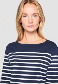 Tamsiai mėlynas dryžuotas marškinėliai su baltais horizontaliais dryžiais, apykaklė su apvaliu iškirpimu ir ilgomis rankovėmis. Audinys atrodo minkštas su lygiu tekstūru.